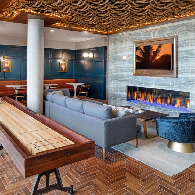 Rivage Apartments - Clubroom with Shuffleboard, Couch, TV, and Fireplace